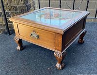 Front and side angle view of square wooden side table with carved legs and claw feet, showing drawer front and brass pull.