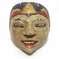 Front view of carved wooden South Asian dancing mask with painted facial details and signs of paint wear.