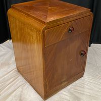 Front and side view of the teak mini bar cabinet showing drawer and door with rounded knobs and wood grain geometric veneer pattern.