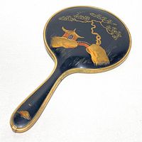 Front view of the hand mirror showing the painted Bakelite back with an Asian-inspired scene including a pagoda, tree, and rocks in gold, red, blue, and green.