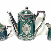 Front and detail view of dark green ceramic teapot with sterling silver overlay showing floral and vine Art Nouveau design, silver lid, stylized handle, and spout