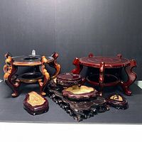 Front left angled view of the group of 8 carved wood and natural wood slab display stands on a black surface.