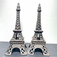 Front-facing view of two cast iron Eiffel Tower statues placed side by side on a flat surface against a white background.