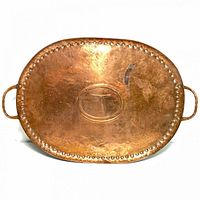 Full view of the oval hand hammered copper tray showing the studded border, two handles, and general surface wear.