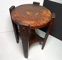 View of the vintage walnut plant stand showing round top, three legs, and base shelf with wood grain and wear.