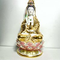 Front view of the full Buddha statue seated on a lotus base with gold and pink details and Chinese characters on base.