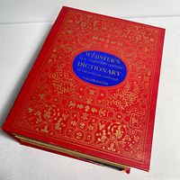 Front cover of the dictionary showing red hardcover with ornate gold embellishments and blue oval title label.