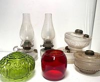 Full lot of oil lamp parts arranged on white background, showing variety of clear glass lamps with chimneys and colored glass parts