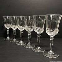 Set of six clear crystal champagne glasses lined up against a black background showing fluted bowl design and faceted stems.