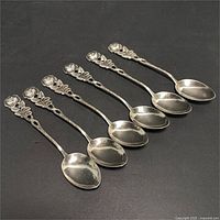 Set of 6 silver plated spoons with detailed rose motif on handles, arranged in a row showing the fronts.