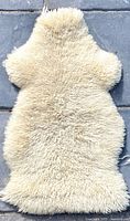 Top-down view of cream white natural sheep skin rug laid flat on stone floor.