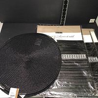Set of 10 round black placemats stacked with 3 black bejeweled table runners in original packaging with branding visible.
