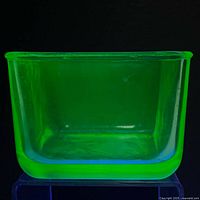 Front-facing view of a square uranium glass refrigerator dish glowing bright green under UV light.