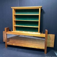 Two wood display cases placed one on top of the other against a dark background. The lower is a darker wood rectangular glass-front case with side handles; the upper is light wood with shelves and green felt backing.
