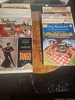 Photo of a selection of vinyl LPs including tangos, Gilbert & Sullivan overtures, and festival music sets on a wooden table.