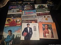 Top-down photo showing approximately 20 vinyl album covers laid out featuring Christmas albums from various artists including Elvis Presley, Whitney Houston, Glen Campbell, and others.
