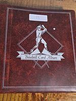 Closed cover of the red baseball card album with white illustration and lettering.