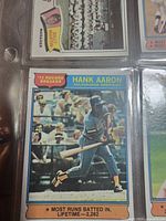 Close-up photo of Hank Aaron baseball card in the album, showing player batting, text indicating '75 Record Breaker and Most Runs Batted In Lifetime - 2,622.'