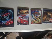 Front view of four Blu-ray disc cases arranged side by side: Cars, Cars 2, Fire & Rescue (sealed), and Batman Begins (sealed).