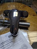 Faucet top view showing chrome finish and black lever handle on a wooden table with installation instructions underneath.