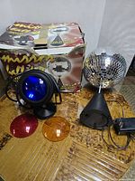 Photo of the disco ball, black spotlight with blue light cover, power adapter, and three colored covers laid out with original box showing.