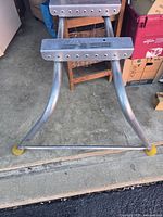 Full view of metal ladder brace attachment with curved arms and rubber end caps for ladder stabilization.