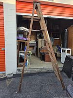 Front view of wooden A-frame ladder standing outside in front of storage units.