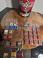 Photo showing Coca Cola NASCAR official souvenir banner and assorted vintage matchbooks laid out on a table.