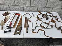 Old rusty hand tools including trowels, saws, and metal star-shaped tool on a white table.