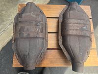 Two rectangular exhaust mufflers with rust and wear, viewed from top on a wooden surface.