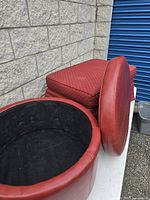 Photo showing the interior of the round ottoman with the cushioned lid removed, displaying black fabric lining inside for storage.
