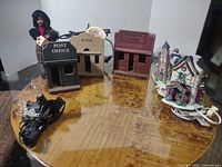 Five lighted village buildings made of wood and ceramic/porcelain, with attached cords, on a round table.