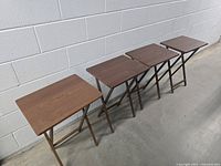 Four vintage wood folding TV dinner tables aligned side by side, showing size comparison and condition.