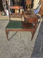 Front view of vintage wooden telephone bench with green cushioned seat and carved backrest, attached side table to the right.