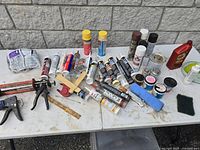 Overall lot showing multiple tubes of plumbing adhesives, sealants, compounds, caulk guns, and some hand tools on a table.