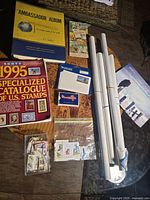 Overview photo showing multiple items including Ambassador album, 1995 Scott Specialized Catalogue, small stamp booklets, multiple rolls of posters, and plastic bags with stamps.