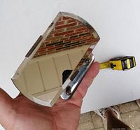 Side view showing beveled mirror glass and chrome mount held in hand with tape measure for scale.