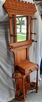 Front view of antique wooden hall stand showing mirror, peg hooks on sides, pull-out drawer, and umbrella holders below