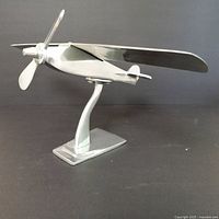 Side view of the silver aluminum airplane display piece on a black background showing the propeller and base stand.