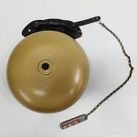 Side view of the beige/tan metal fire/school bell with black mounting bracket and pull chain with tag '333'.