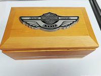 Closed wooden jewelry box with Harley Davidson metal emblem on lid showing 1903-2003 winged logo.