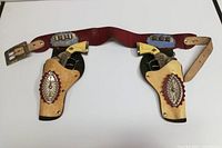 Full view of the double holster belt holding two toy cap guns, showing the condition of leather and metal components