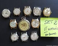 Front view of 11 watches including 10 wristwatches without bands and 1 pocket watch, showing dials and brand names like Bulova and Saga.