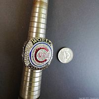 Ring displayed on a ring sizing tool next to a quarter to show size and details. Front face features the Chicago Cubs circular logo with the words 'WORLD CHAMPIONS'.
