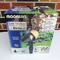 Box showing product packaging with branding and features: Moonrays Low Voltage Metal Landscape Lighting Kit with 4 black finish lights, 20 watt fixtures, installs in less than an hour.