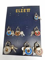 Front view of display card with six Elzett padlocks mounted and several keys attached. One padlock is detached but present.