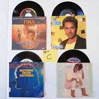 Four 45 RPM records visible with original picture sleeves, front side facing up showing sleeves and vinyl partially out.
