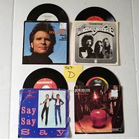 Top view showing all four 45 RPM records with original picture sleeves, displaying front covers for John Fogerty, Edward Bear, Paul McCartney & Michael Jackson, and Bob Seeger.