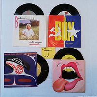 Set of four 45 RPM vinyl records shown with original picture sleeves visible, colorful artwork for each artist including Barbara Mandrell, Ordinary People, Bruce Cockburn, and The Rolling Stones.