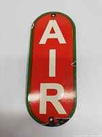Front close-up of porcelain sign with 'AIR' in white on red and green border, showing chips and wear.